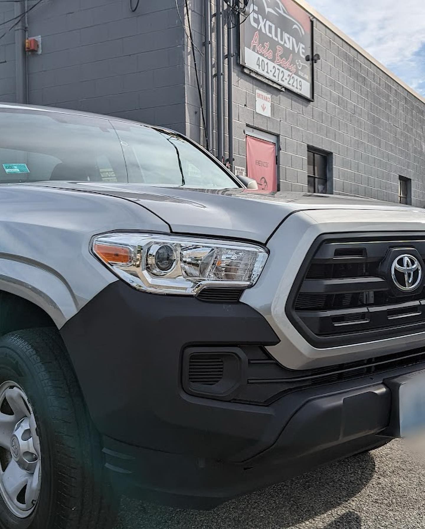 A silver toyota tacoma truck is parked in front of a building.