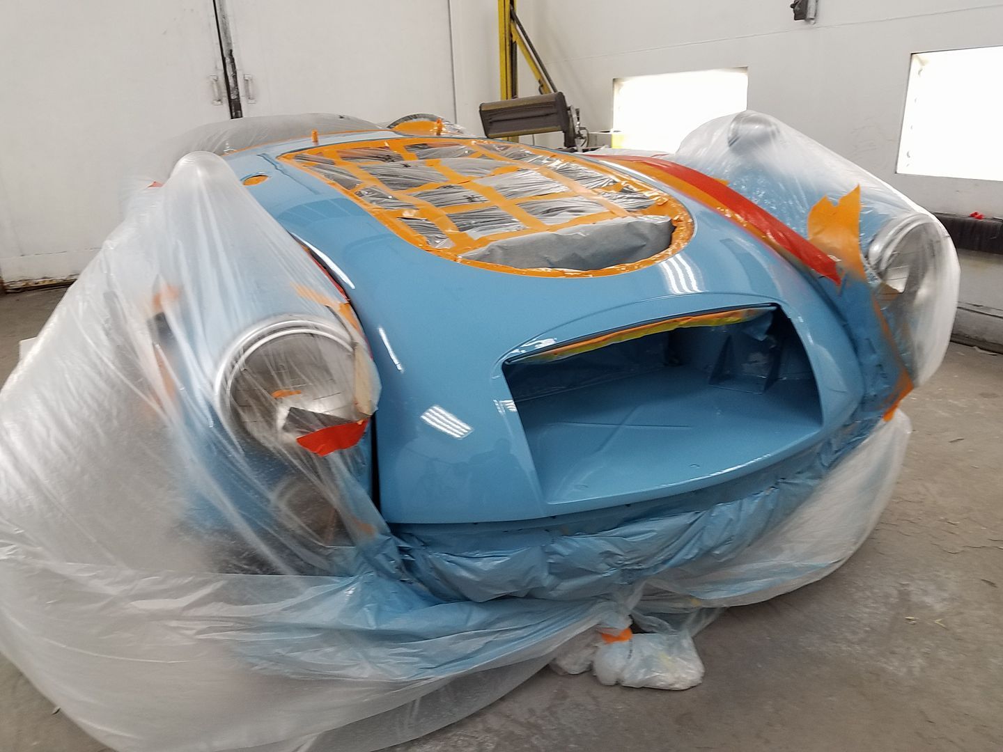 A blue car is wrapped in plastic in a garage.