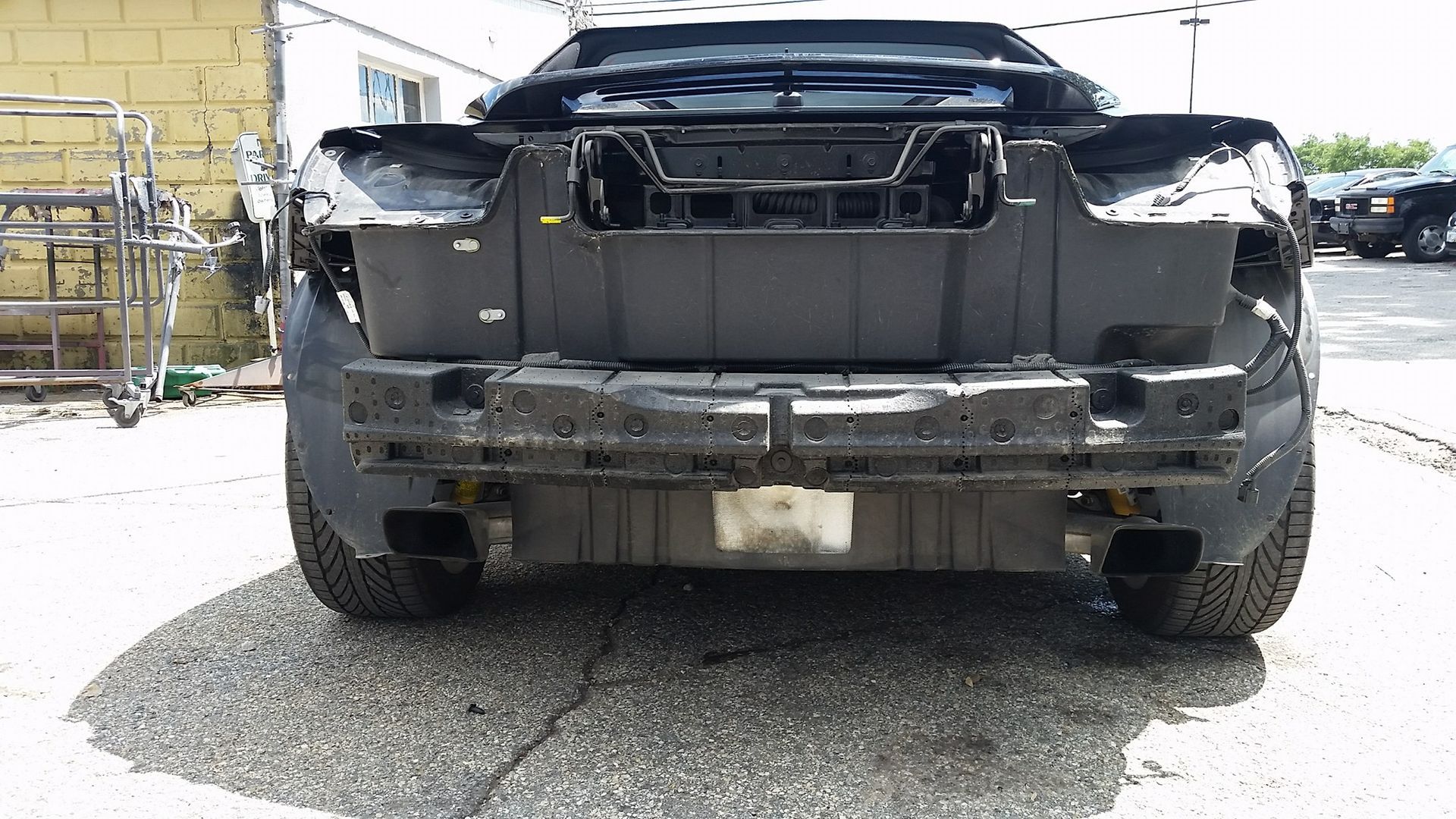 A black car with the rear end removed is parked in a parking lot.