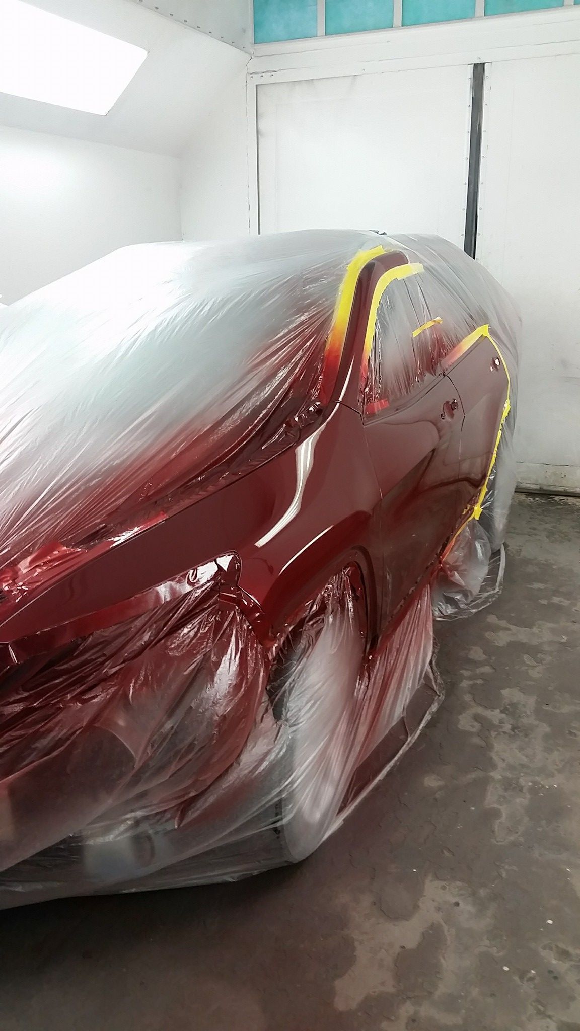 A red car is wrapped in plastic in a garage.