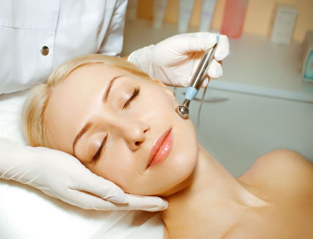 Person receiving facial treatment with a handheld device, lying on a spa bed with eyes closed.