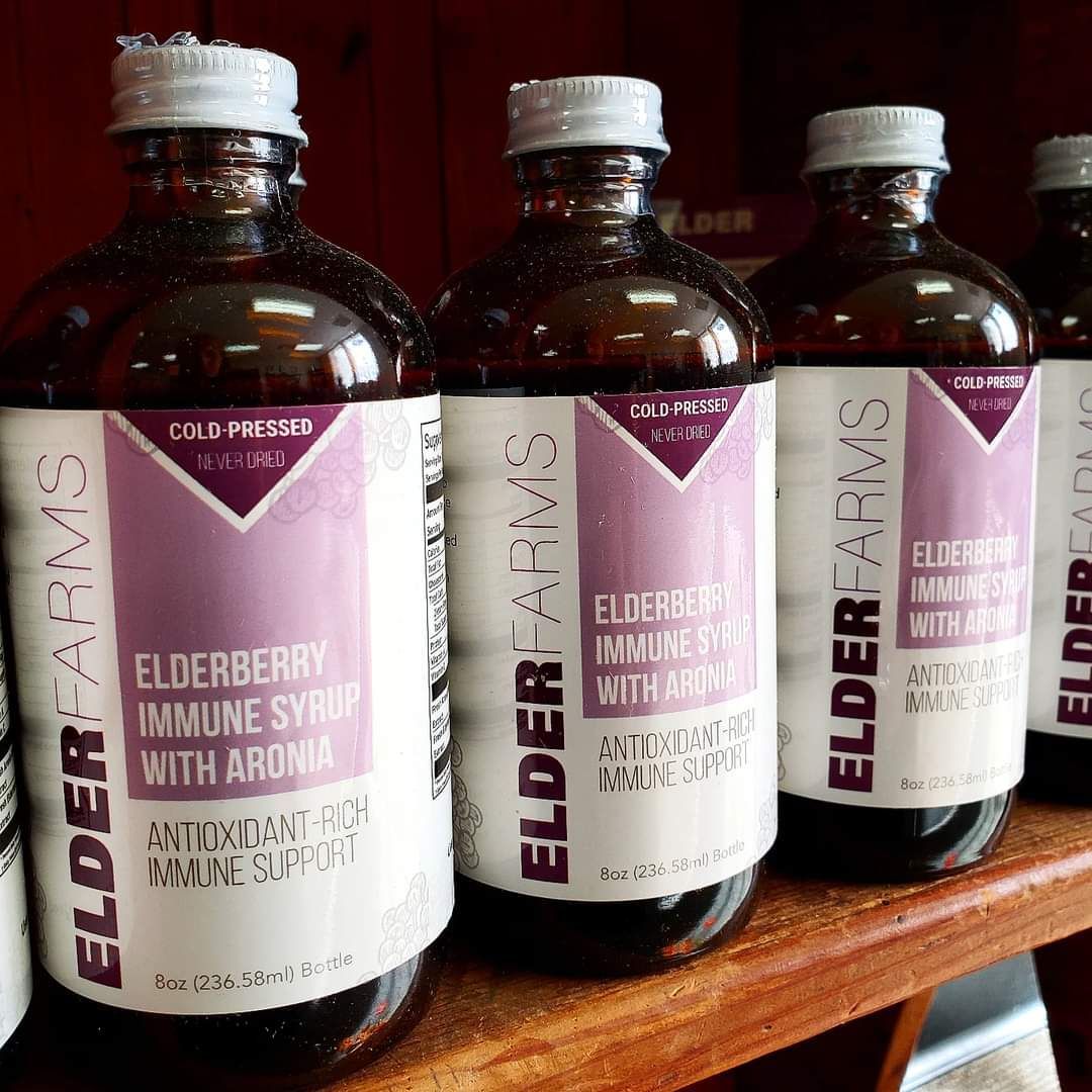 Bottles of Elderberry Immune Syrup with Aronia on a shelf, labeled with white and purple stickers.