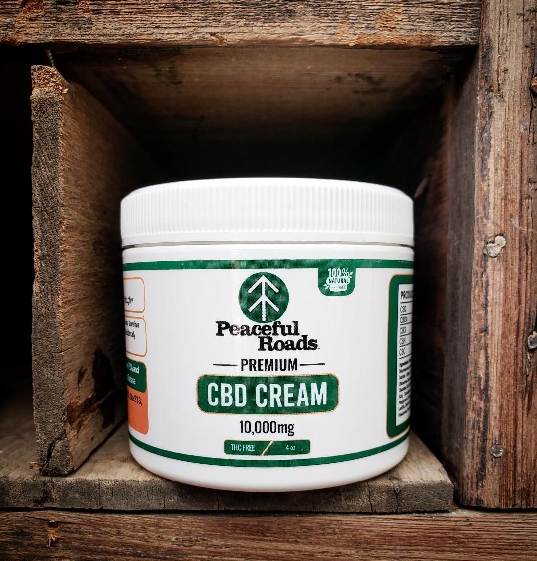 White jar of Peaceful Roads CBD cream, 10,000mg, on wooden shelf.