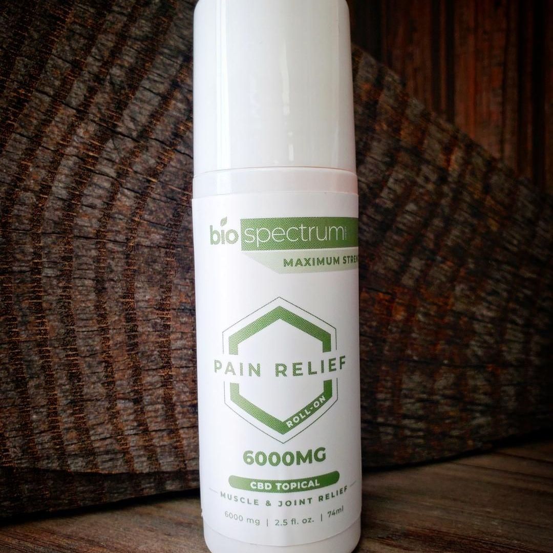 Bottle of BioSpectrum pain relief topical cream with 6000mg of CBD, against a textured wooden background.