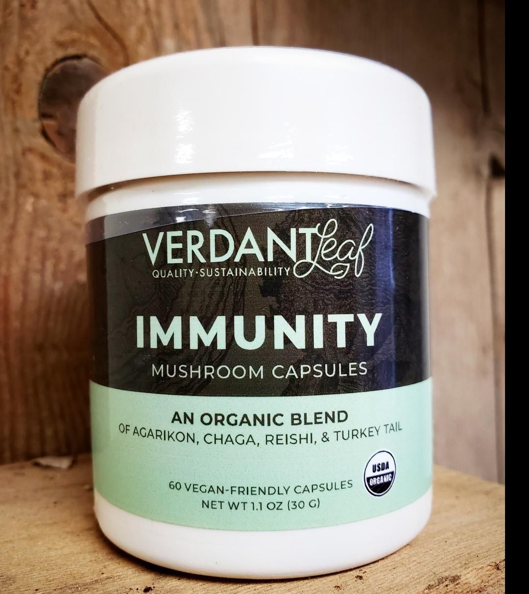 White jar of Verdant Leaf Immunity mushroom capsules with green label on a wooden background