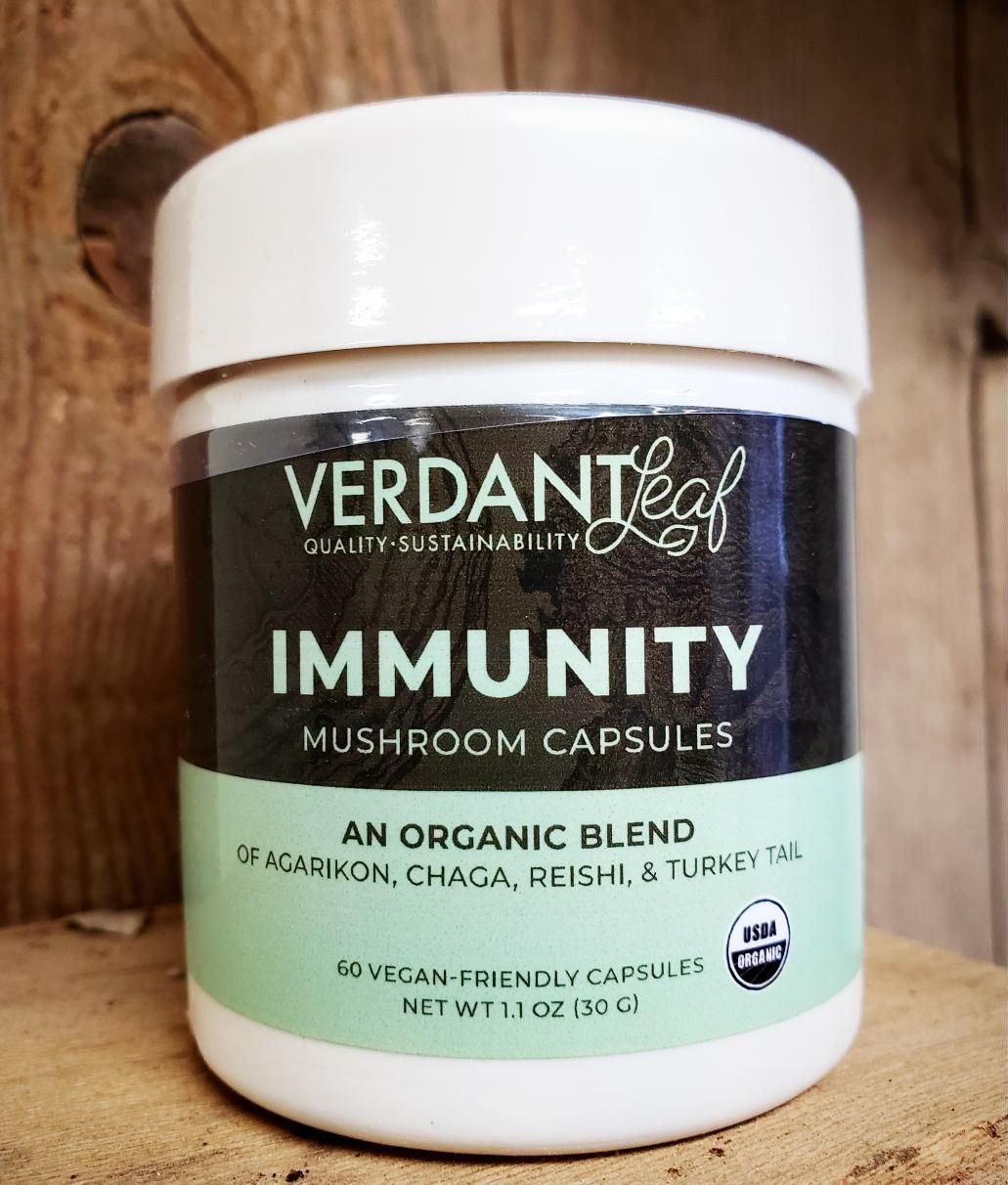 A white bottle of Verdant Leaf Immunity mushroom capsules. It has a black and green label and a wooden background.
