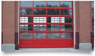 A red garage door with a lot of windows on a brick building.
