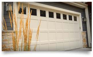 A white garage door is sitting on the side of a house next to tall grass.