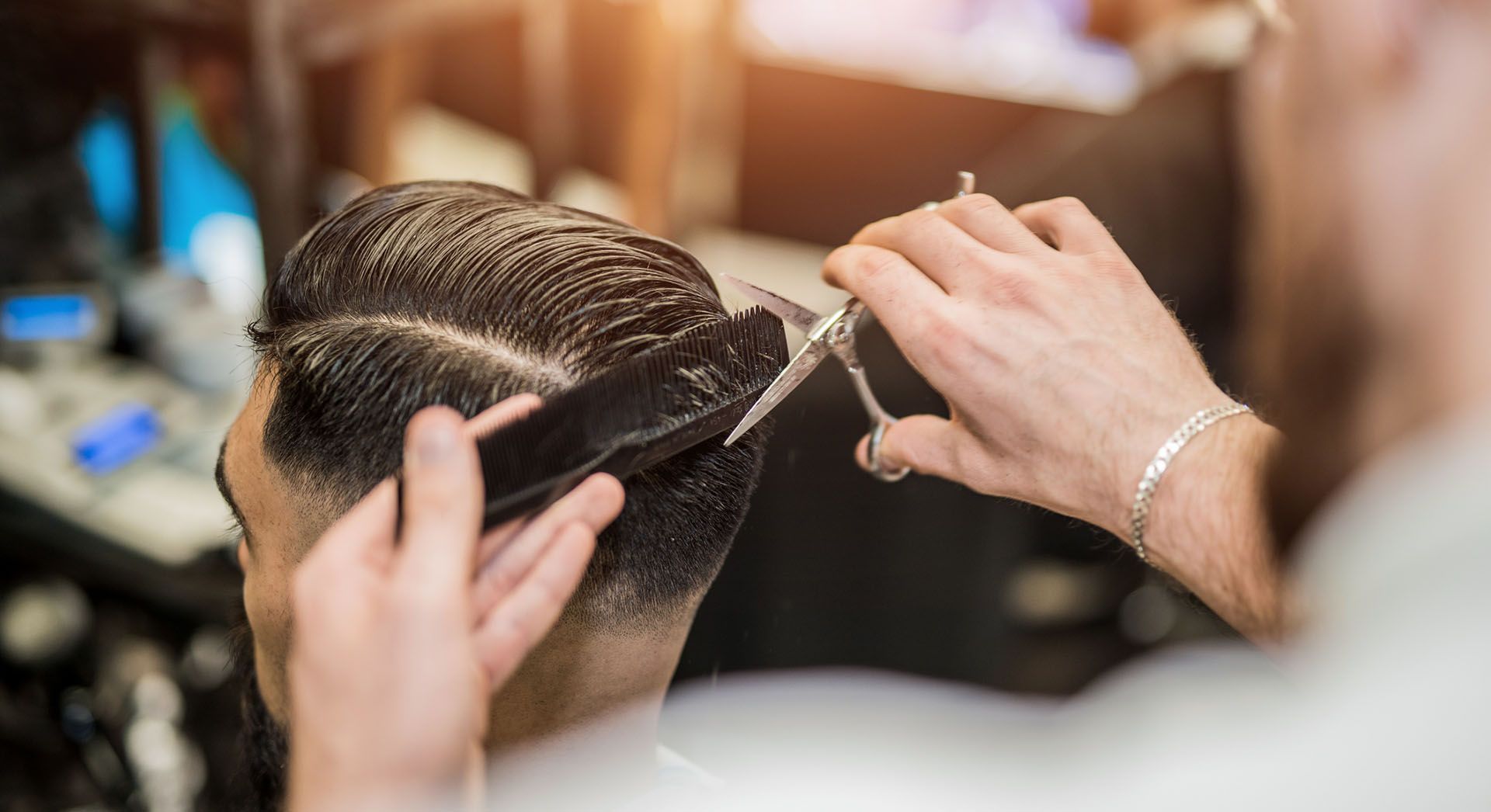 Barber cutting hair with scissors and comb in a shop.