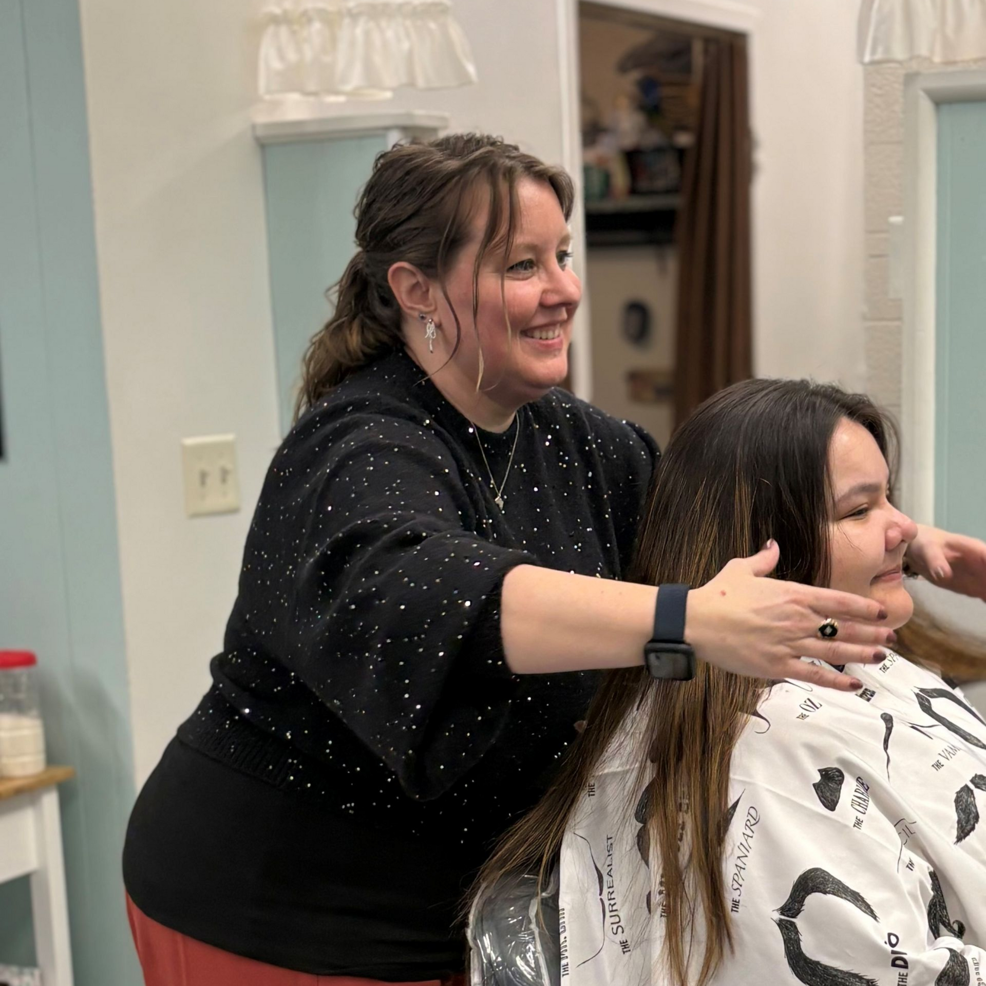 A stylist stands behind a client in a salon, hands raised as if framing the client's hair.
