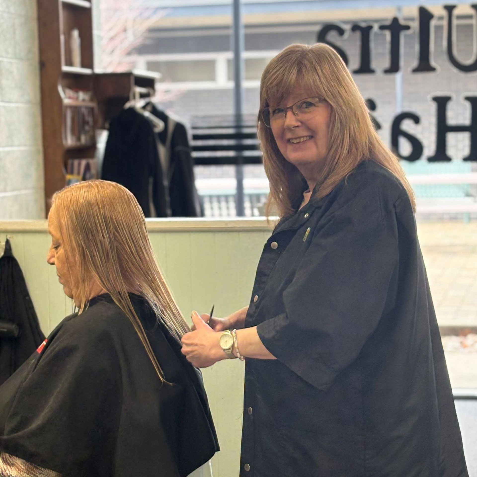A hairdresser works on a client's long, crimped hair in a salon setting.
