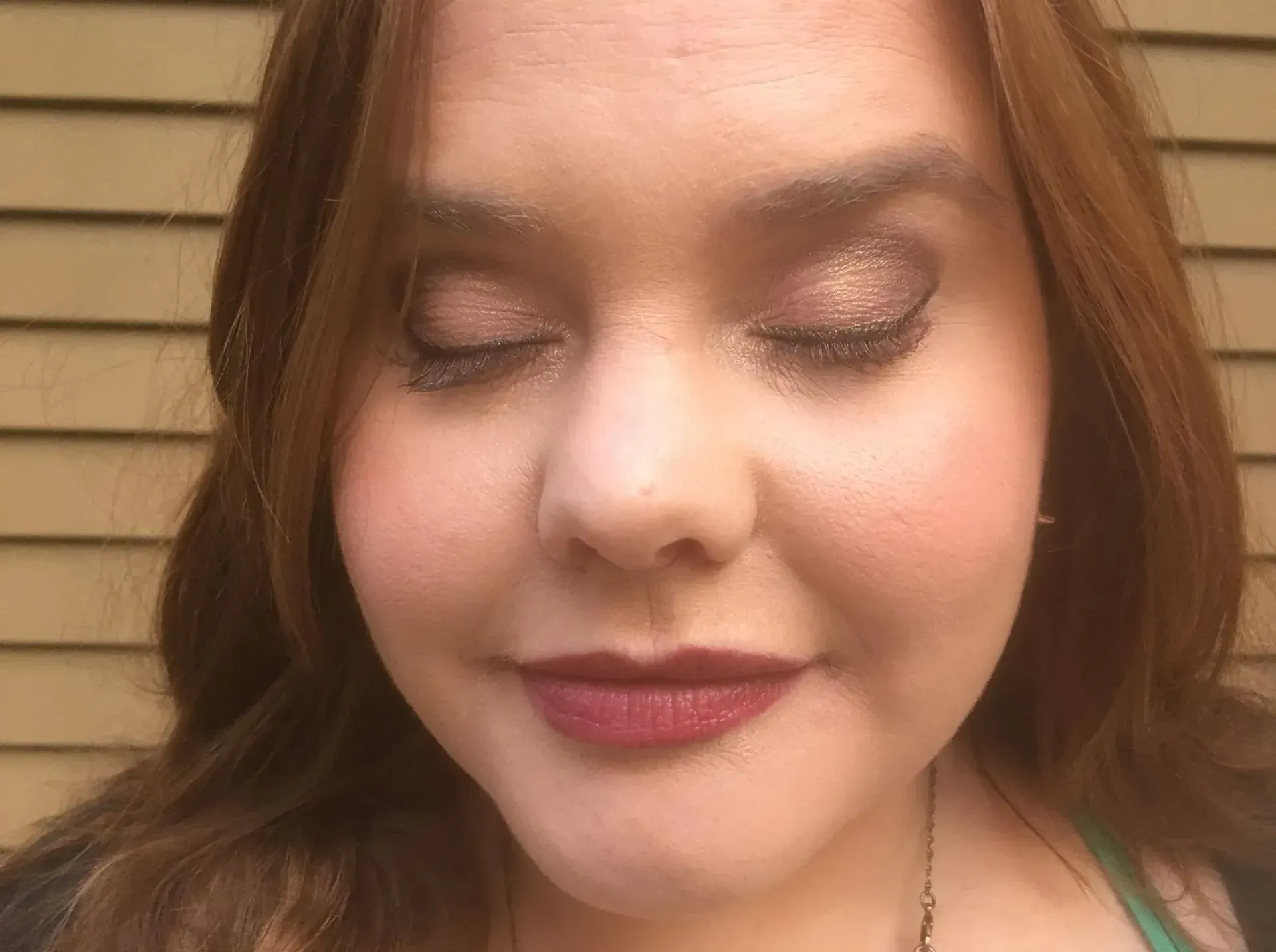 Woman with eyes closed wearing eyeshadow and dark lipstick.