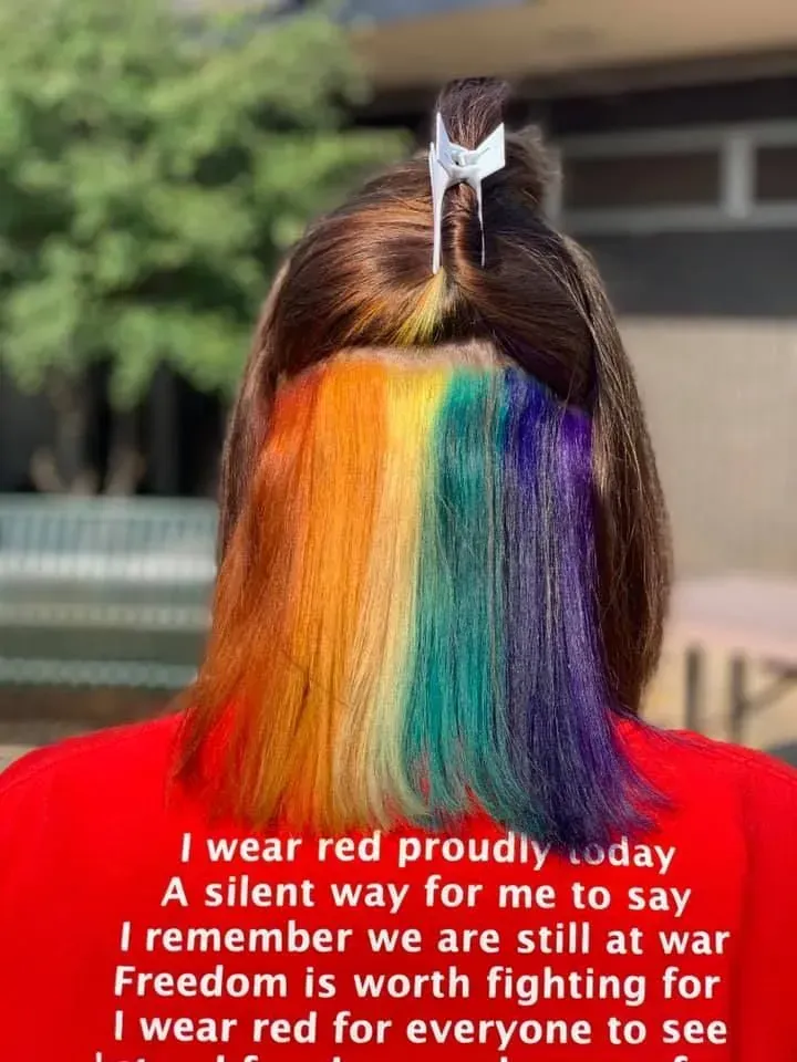 Back view of a person with rainbow-colored hair underneath brown hair, wearing a red shirt.