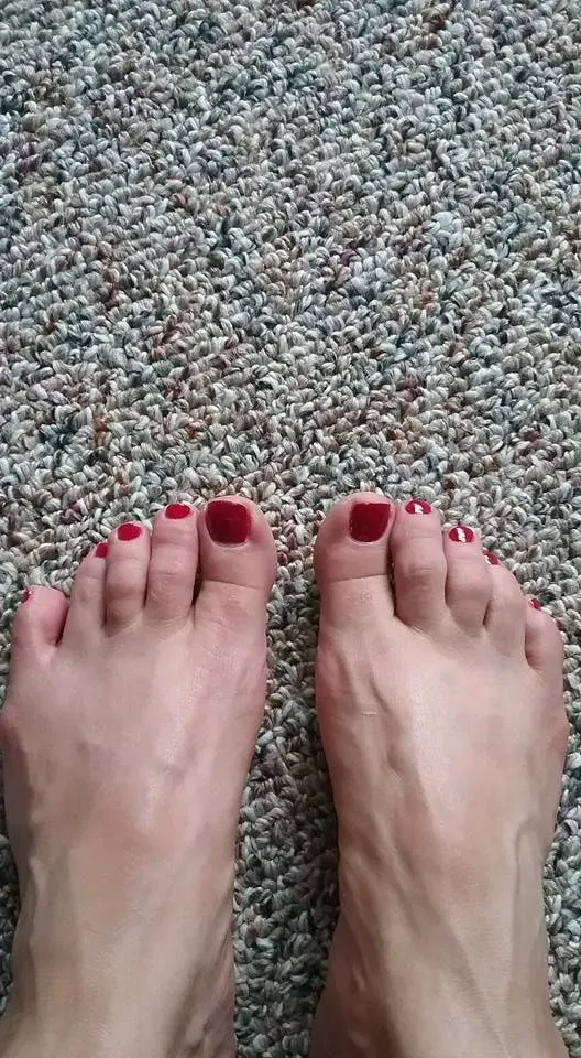 Bare feet with red nail polish on a speckled beige carpet.