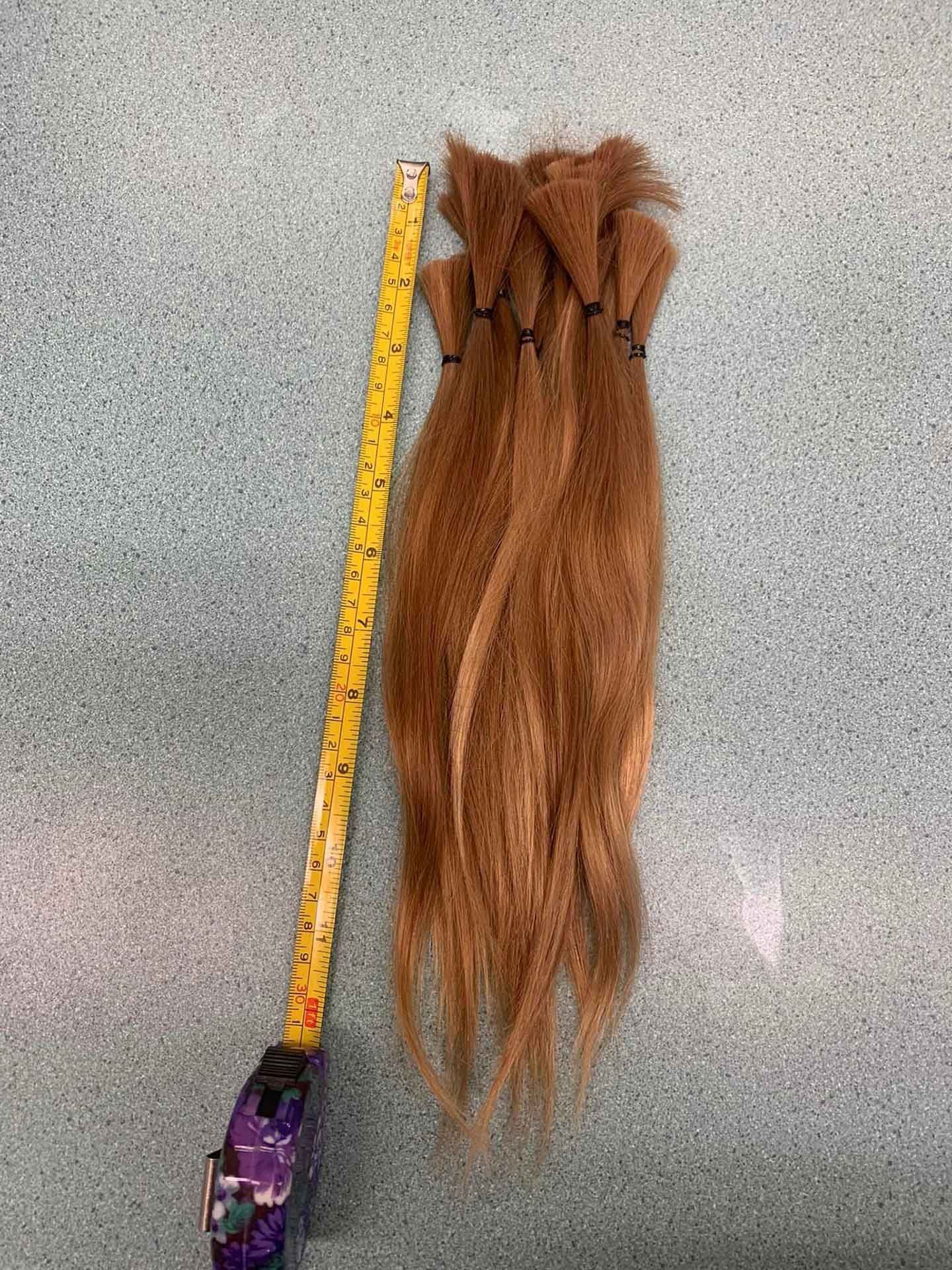 Bundles of brown hair tied with black bands, next to a yellow tape measure on a blue surface.