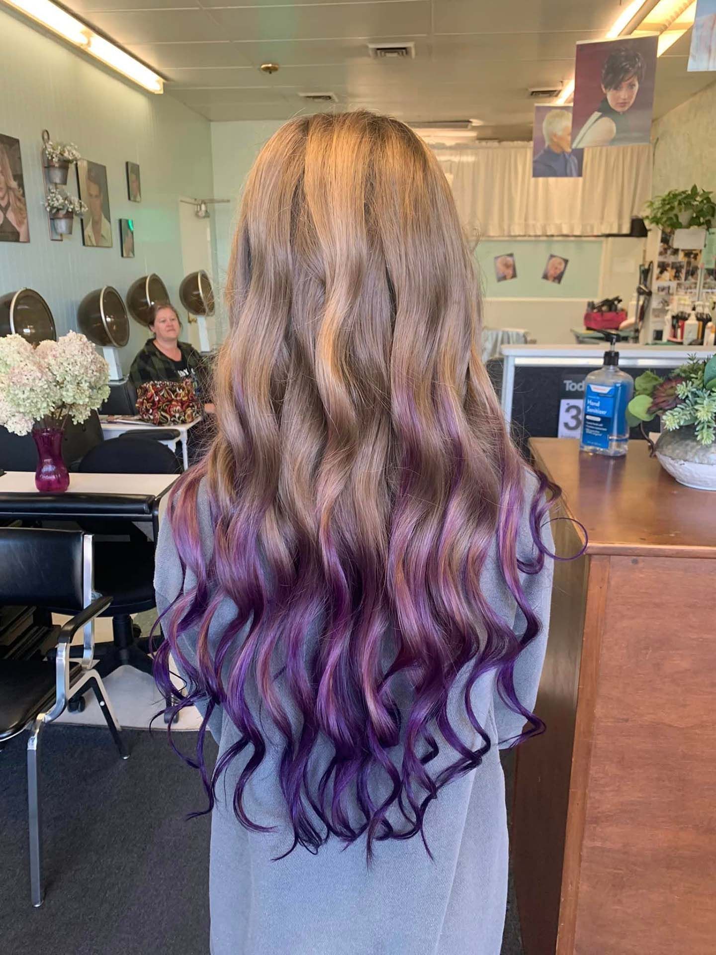 Woman with long, wavy, color-treated hair; blonde to purple ombre. In a hair salon.