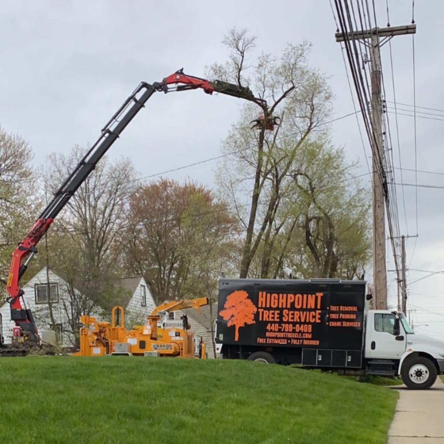 A Highpoint Tree Service truck and crane performing tree removal near power lines on a grassy residential street.