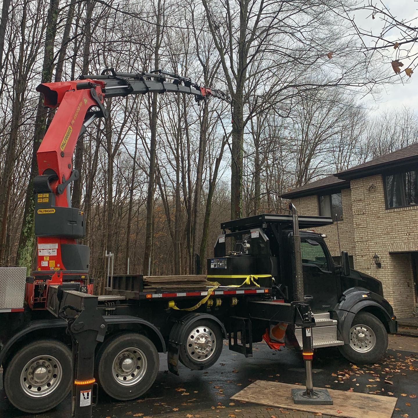 A black flatbed truck with a large red crane arm parked in a wooded residential driveway.