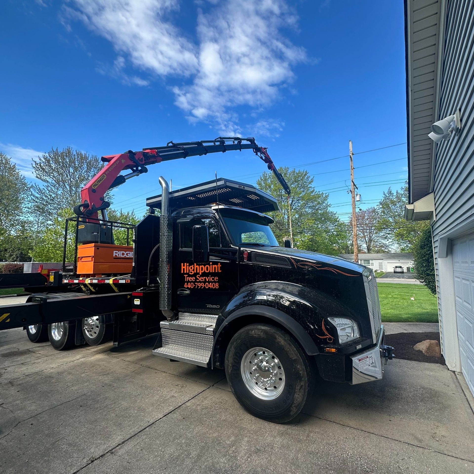 A black Highpoint Tree Service truck with an extended crane arm parked on a concrete driveway next to a house.