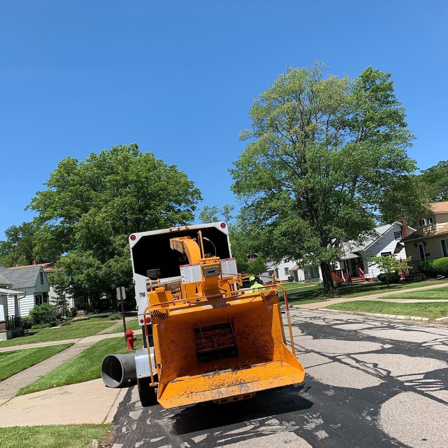 A yellow wood chipper attached to a truck, parked on a residential street under a clear blue sky.