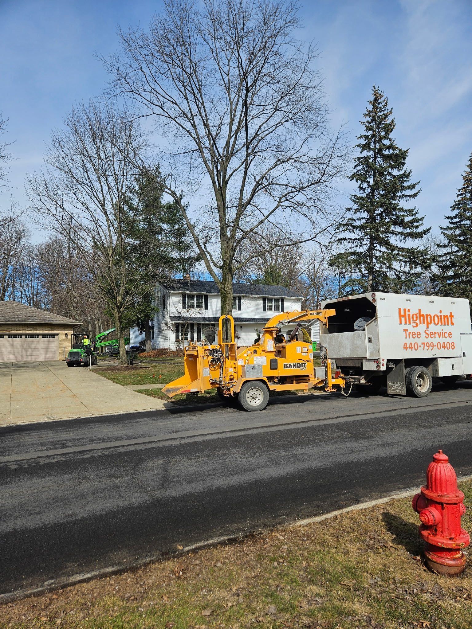 A yellow wood chipper attached to a truck with orange lettering parked on a residential street next to a red fire hydrant.