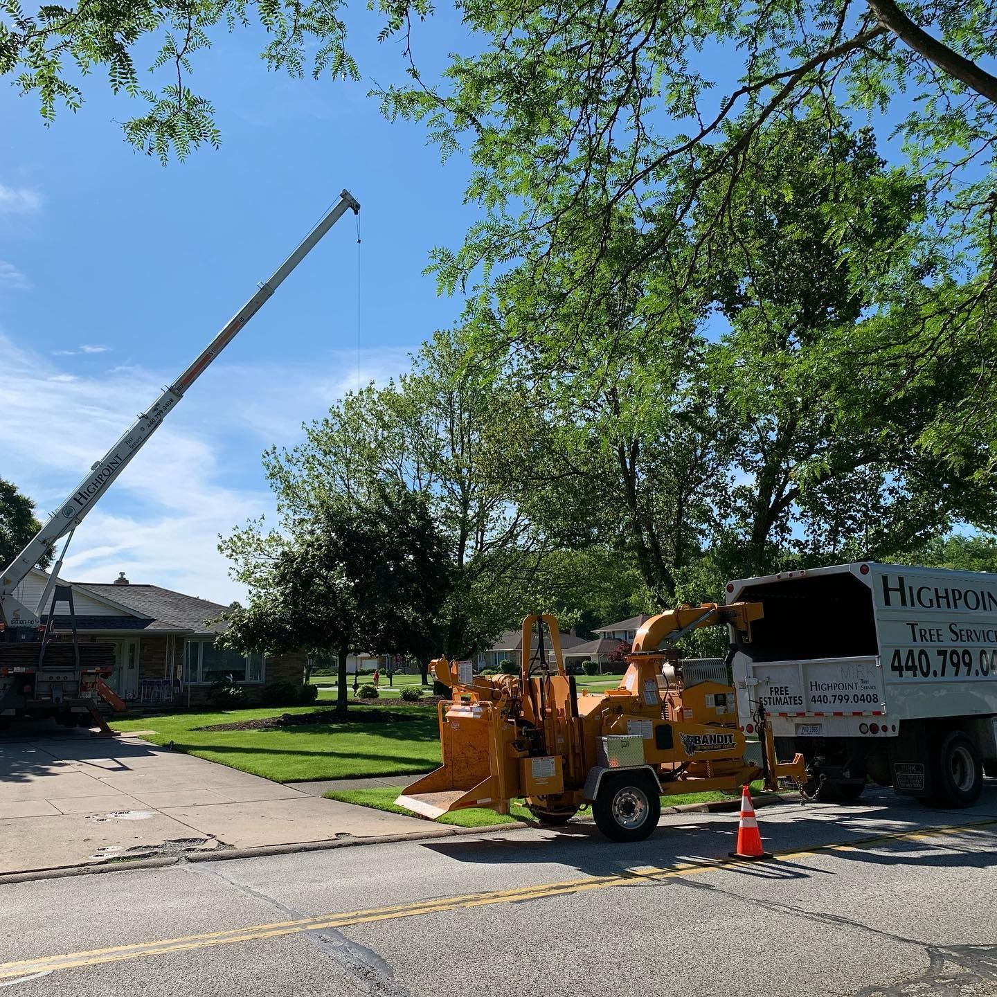 A crane and a wood chipper truck parked on a residential street during a tree removal service on a sunny day.