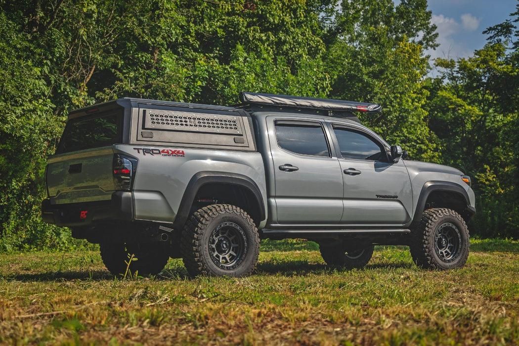Silver pickup truck with off-road tires parked on grass beside trees under a blue sky