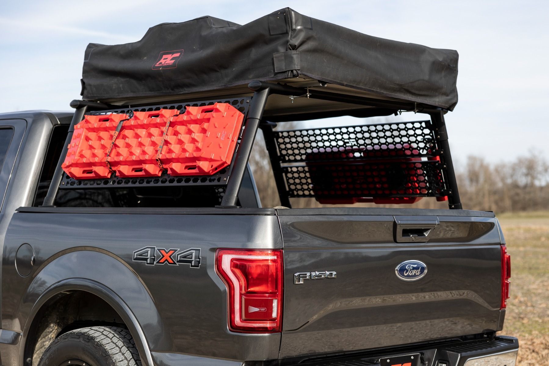 Black Ford pickup with rooftop tent and red cargo bins in the bed, parked outdoors.