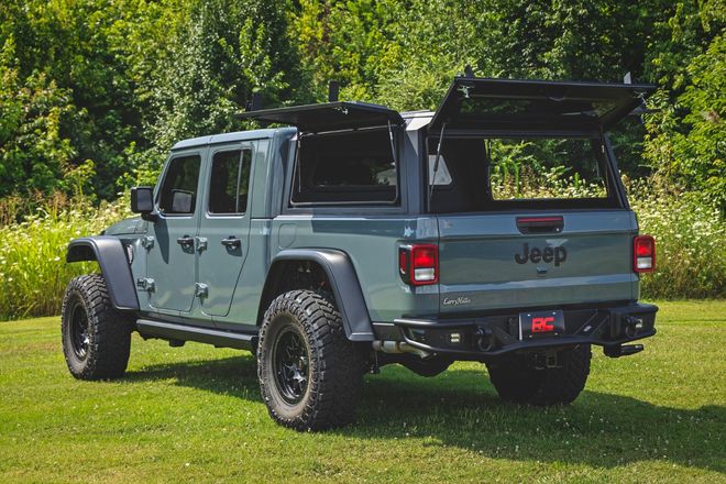 Gray Jeep Gladiator pickup with rooftop camper and open tailgate parked on grass near trees