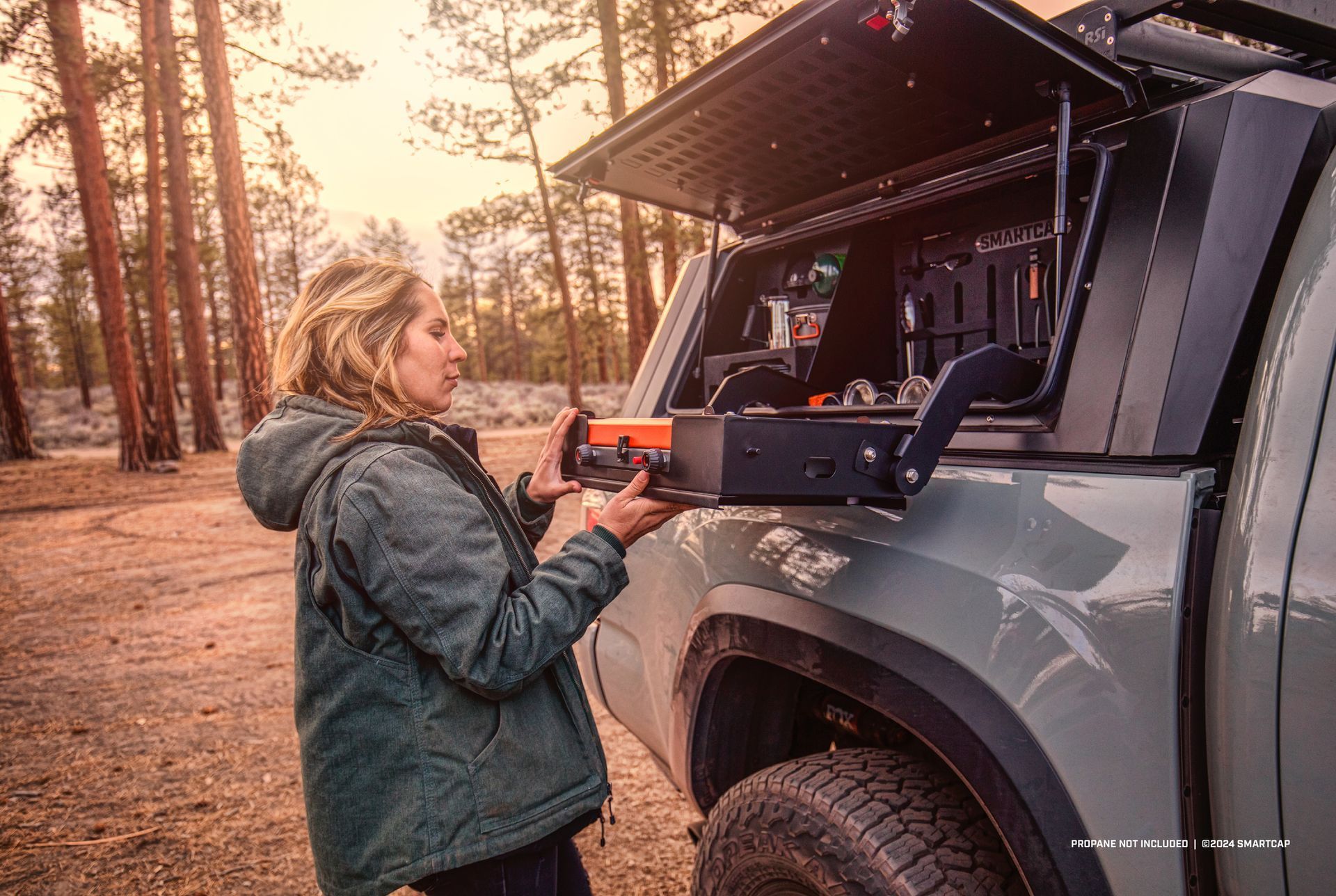 Woman reaching for a drawer in a truck bed camper shell, outdoors.