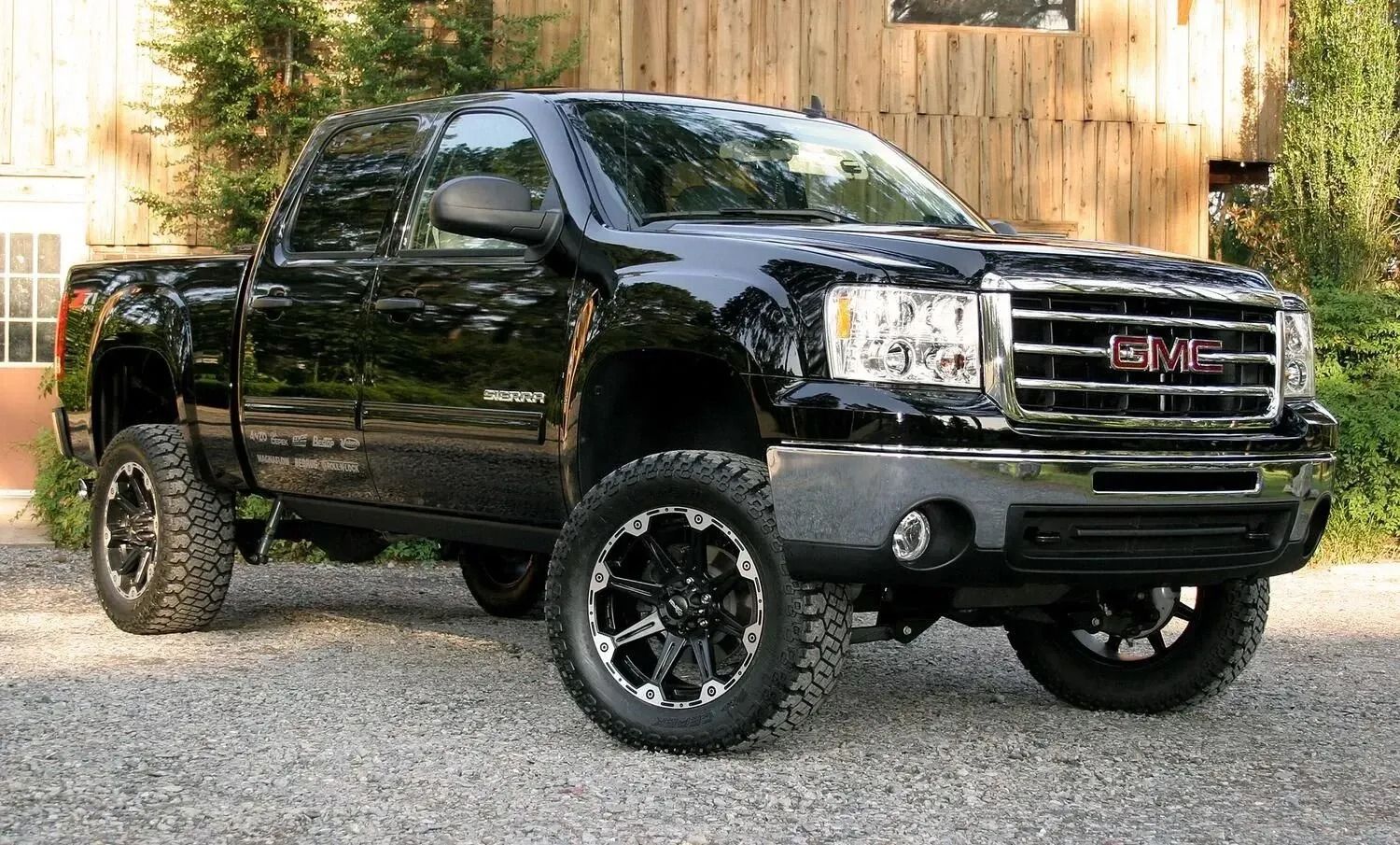 Black GMC Sierra pickup truck parked in front of a wooden building. It has large tires and a lift kit.