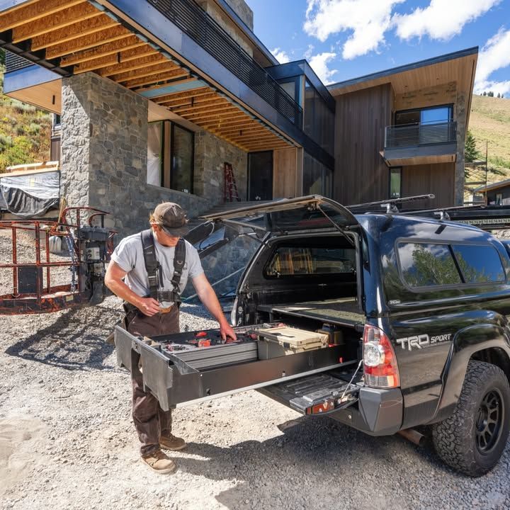 A worker in overalls reaching into a truck bed with slide-out drawers. A modern house is in the background.