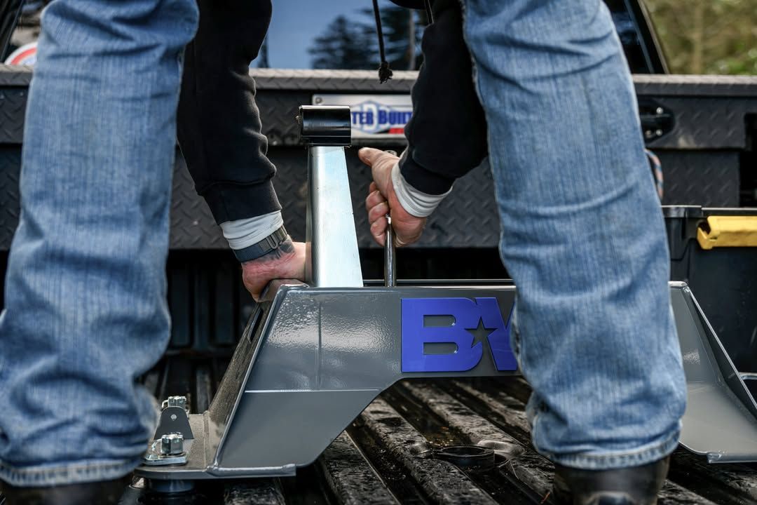Person in blue jeans securing a fifth-wheel hitch in a truck bed using a wrench.