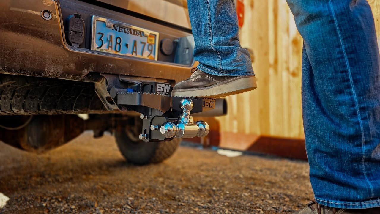 Person stepping onto a truck-mounted step attached to a trailer hitch, outdoors.
