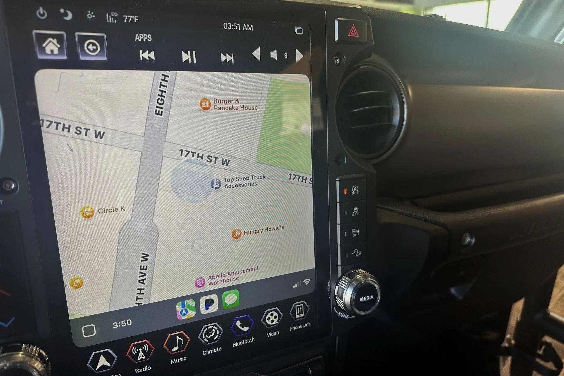 Car dashboard with a large touchscreen displaying a street map, surrounded by buttons and air vents.