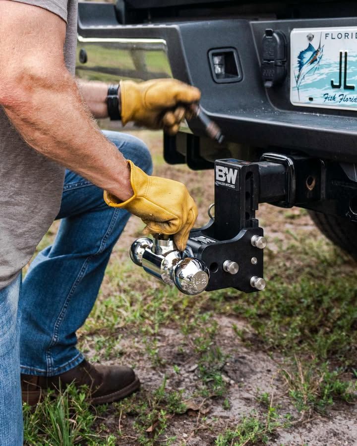 Person in work gloves adjusting a trailer hitch on a black truck, outdoors.