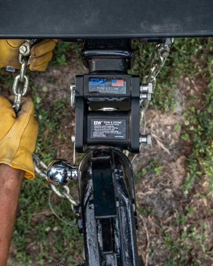 Close-up of a trailer hitch being connected; hands wearing yellow gloves holding a chain.
