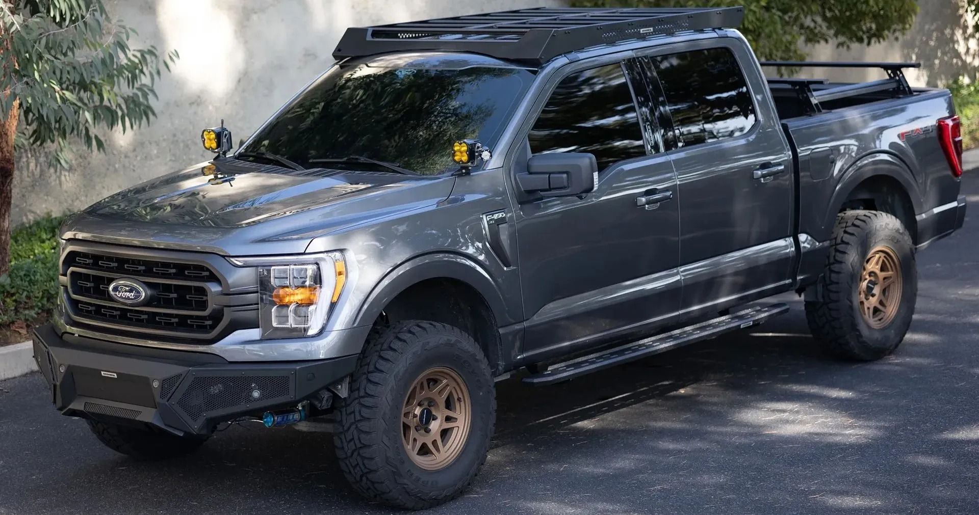 Gray Ford F-150 pickup truck with aftermarket modifications, including off-road tires, brush guard, and roof lights.