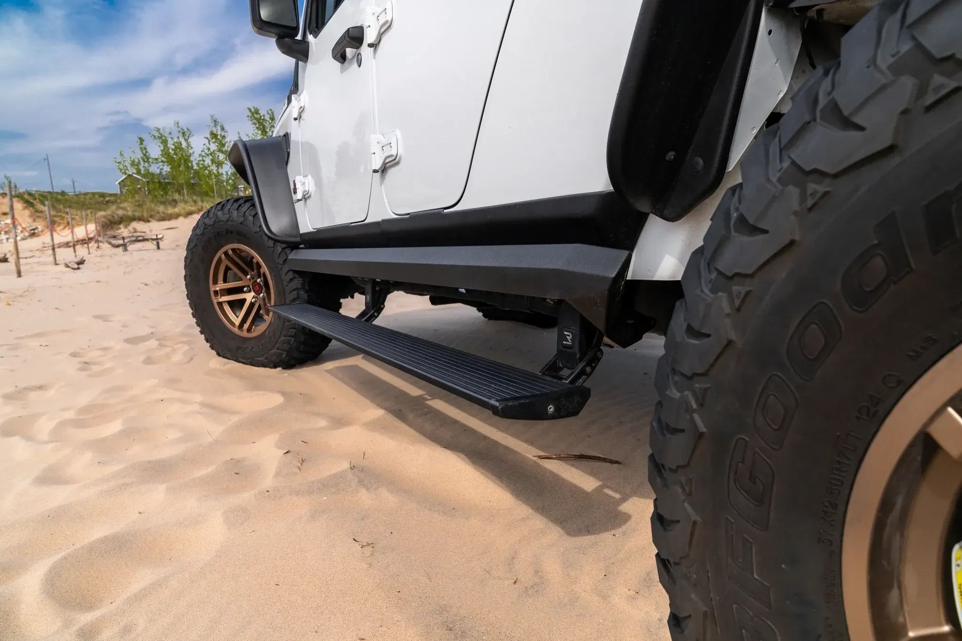 White Jeep with step bar on sand dune, bronze wheels, black fender flares.