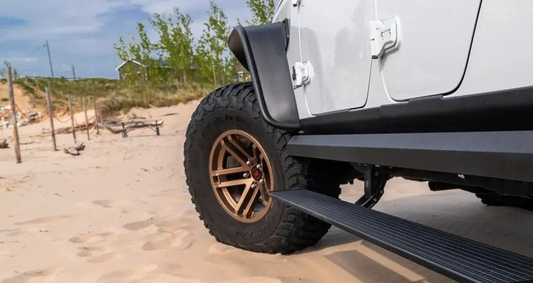 White Jeep with black running board on sandy ground.