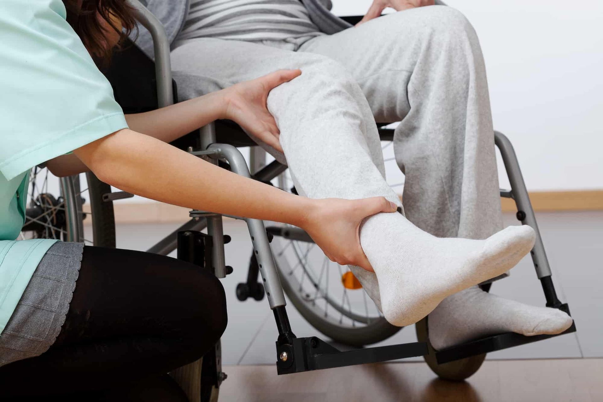 Caregiver helping a person put on a white sock while seated in a wheelchair
