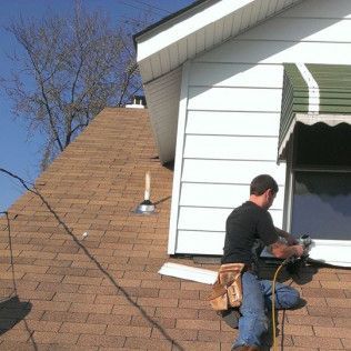 Worker using a power saw on a house roof beside white siding and a dormer