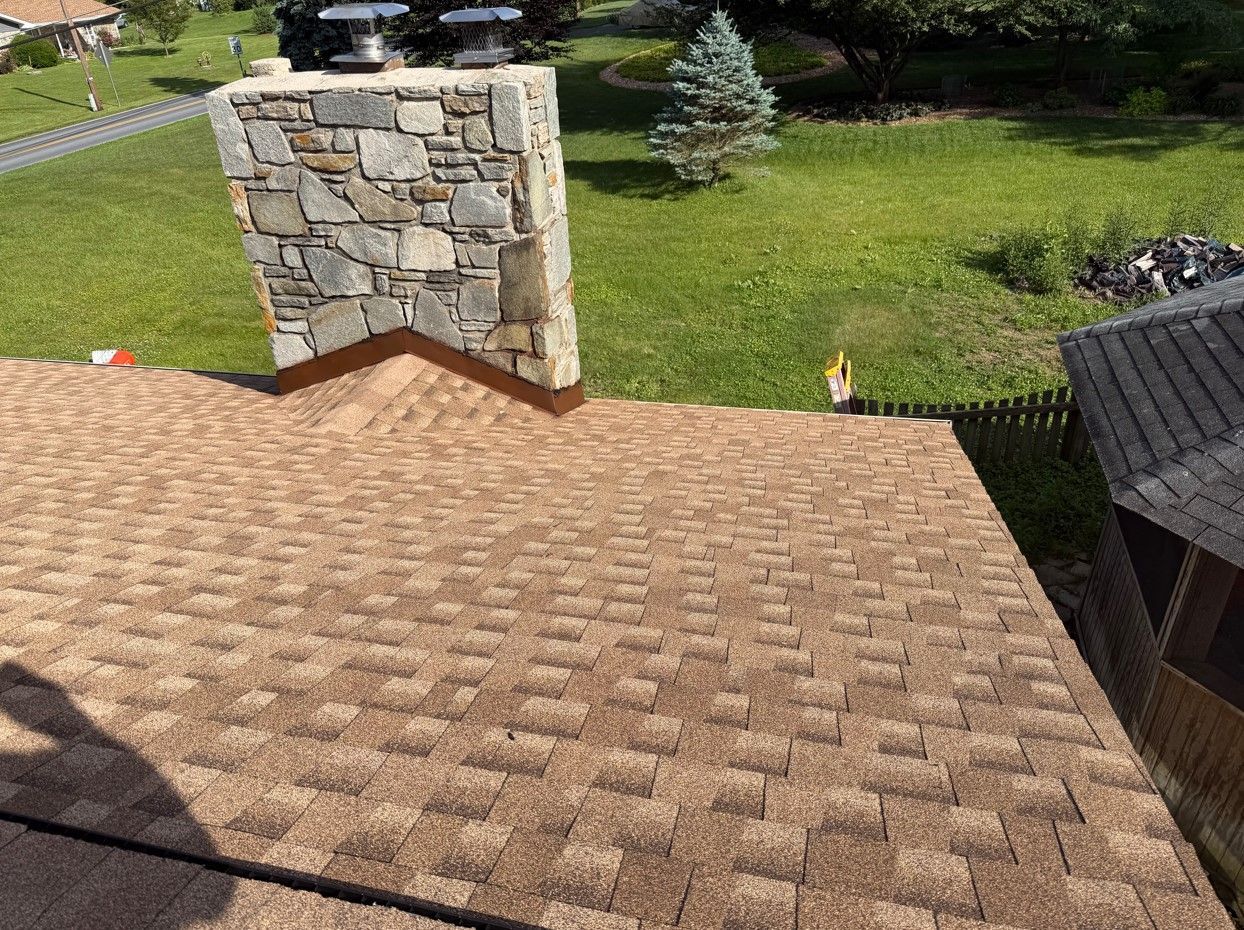 Roof shingles beside a stone chimney with a grassy yard in the background
