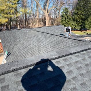 Roofer inspecting a gray shingle roof with trees in the background