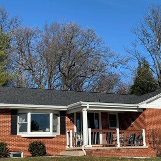 Single-story red brick house with a white porch and dark roof under a blue sky