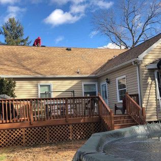 Back deck and stairs on a beige house under a blue sky, with a red-clad worker on the roof