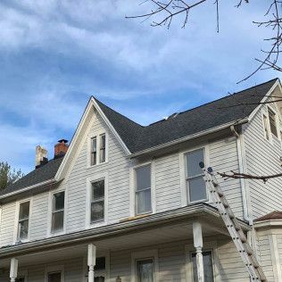 White two-story house with gray roof and porch under a blue sky, with a ladder leaning against the side