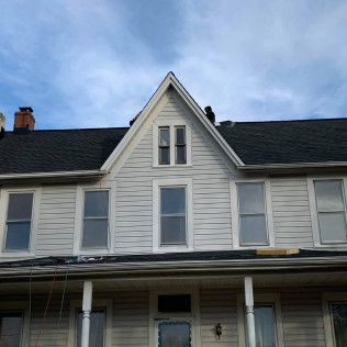 Front view of a gray house with a steep gabled roof and white-trimmed windows under a blue sky