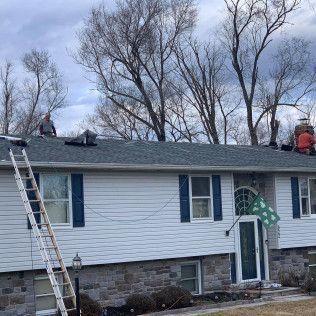 Workers on a house roof with ladders, replacing shingles on a white home with stone siding accents