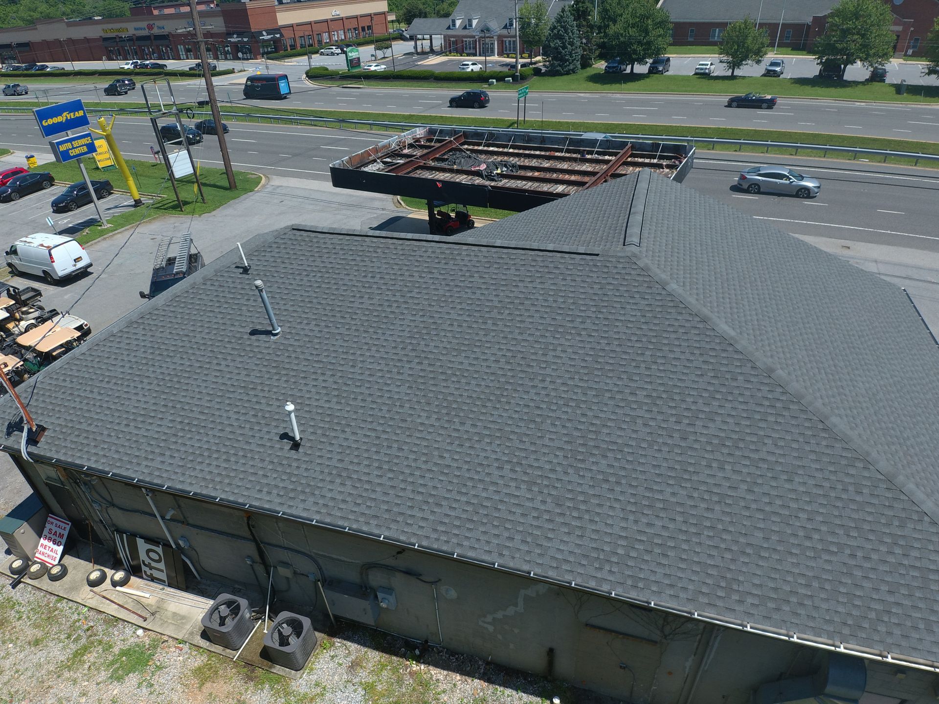 Aerial view of a gray-roofed building beside a busy road and parking lot with a few cars